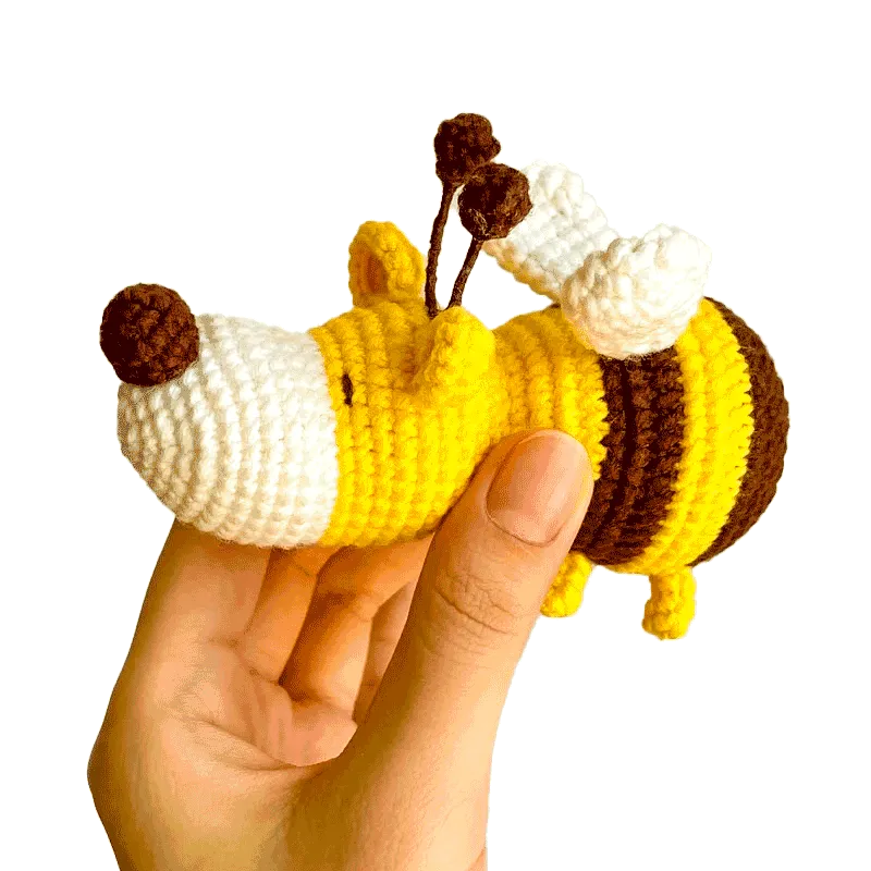 Hand holding a small yellow and brown crochet dog bee pattern with white wings and brown antennae