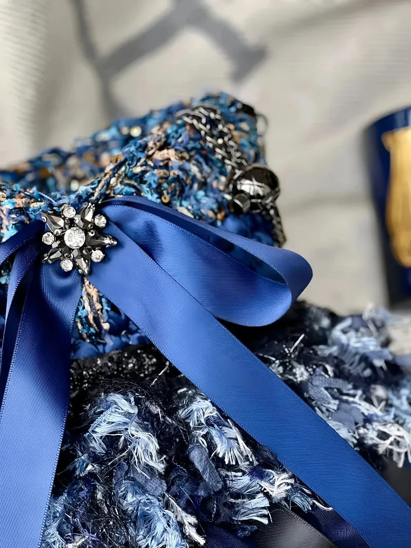 Close-up of a blue crochet handbag pattern featuring intricate stitches and a decorative blue ribbon with a jeweled brooch