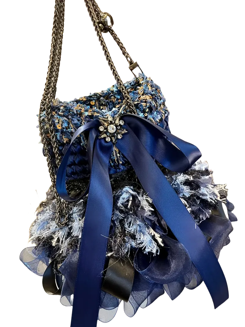 Detailed blue crochet handbag pattern featuring textured yarn and decorative blue ribbon with chain handles
