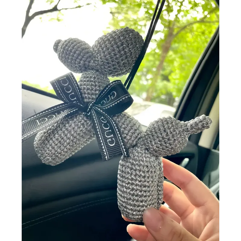 Hand holding a gray crocheted balloon dog with a black ribbon in a car interior showing the crochet balloon dog pattern