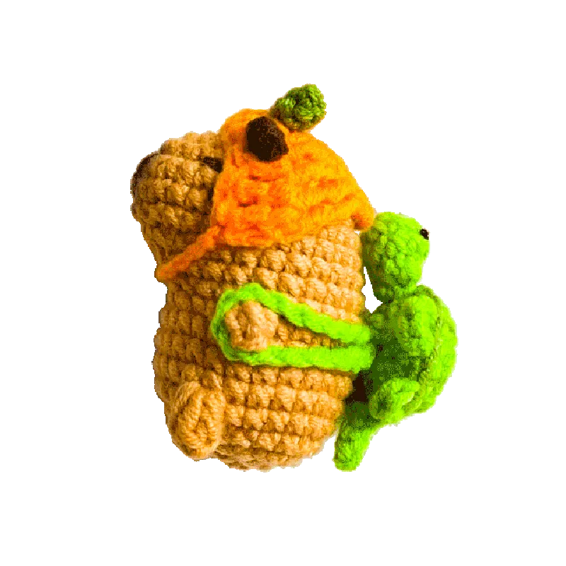 Handmade crochet mini capybara pattern in tan with orange hat and green frog hugging it