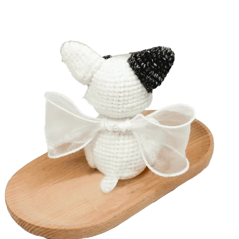 Handmade crochet French bulldog pattern plush figure with white and black yarn details and a white bow on wooden tray