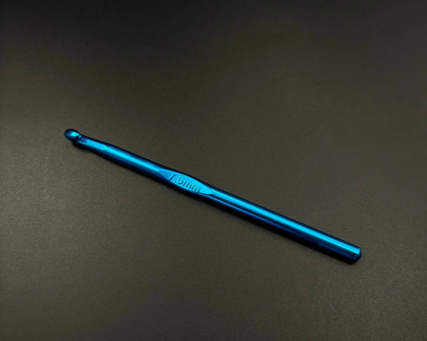 Single blue crochet hook from rainbow aluminum crochet hooks set on black background