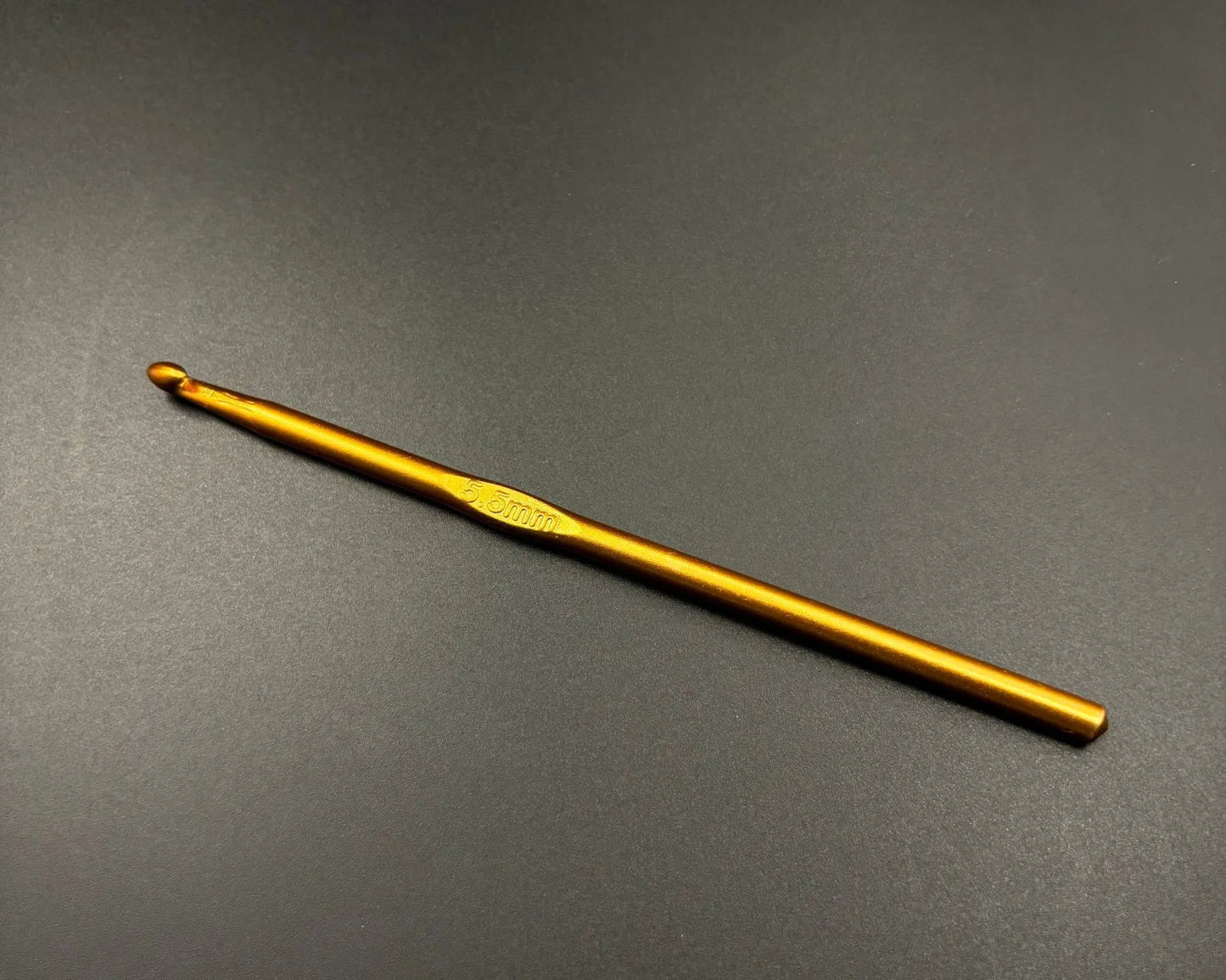 Single gold aluminum crochet hook from a rainbow aluminum crochet hooks set on dark background