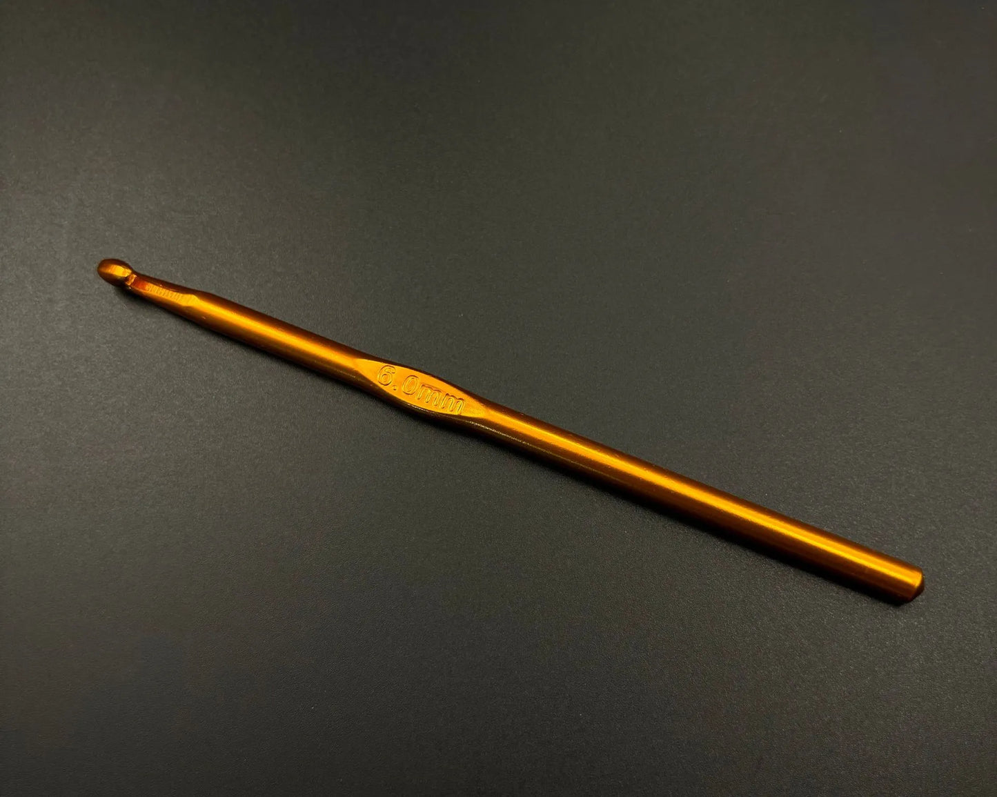 Single orange aluminum crochet hook from rainbow aluminum crochet hooks set on black background
