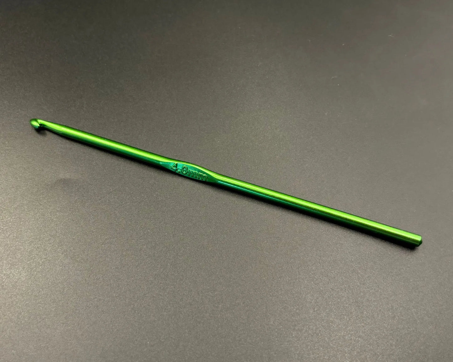 Single green hook from rainbow aluminum crochet hooks set on dark background