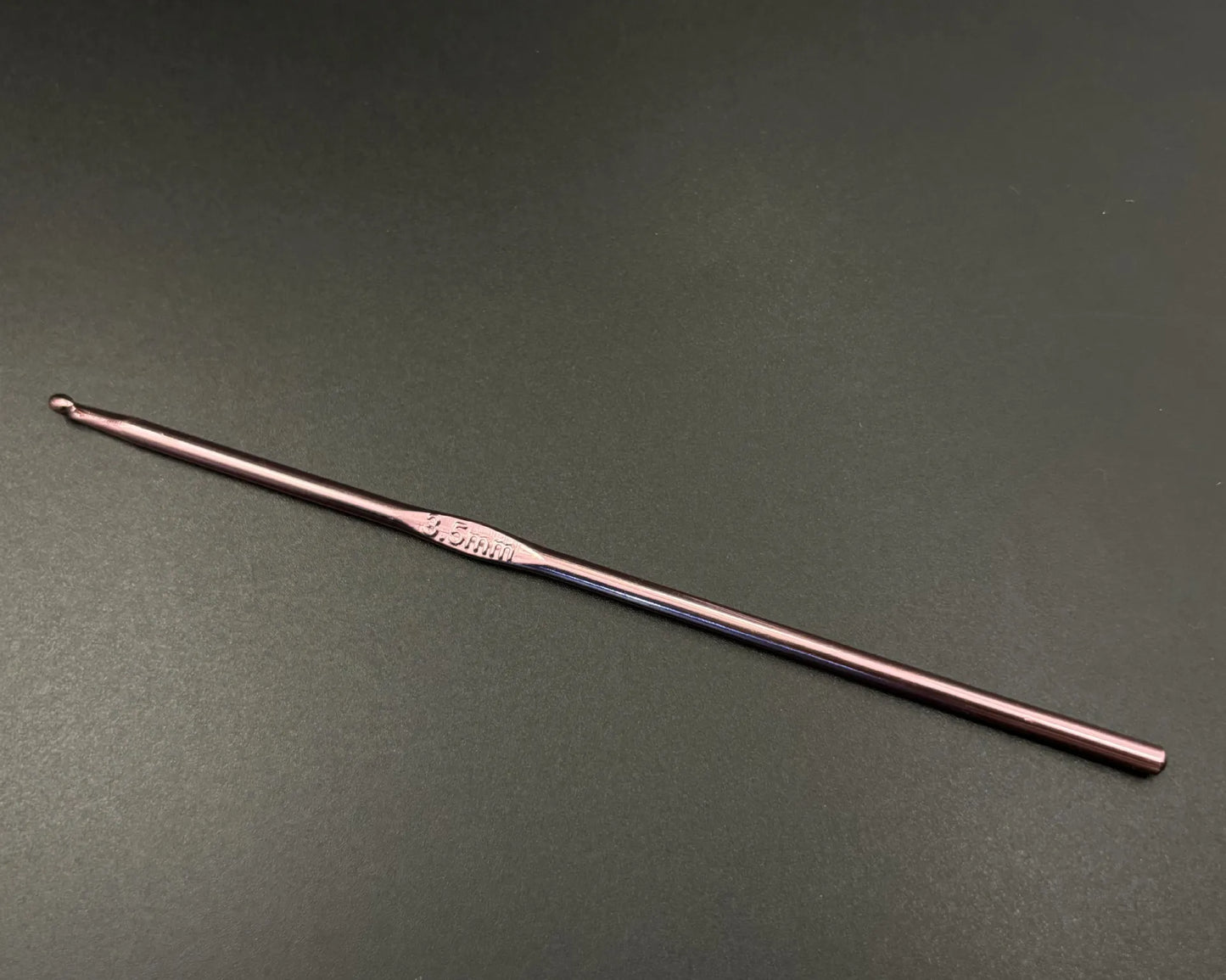 Single rainbow aluminum crochet hooks set in rose gold color with ergonomic grip on dark background