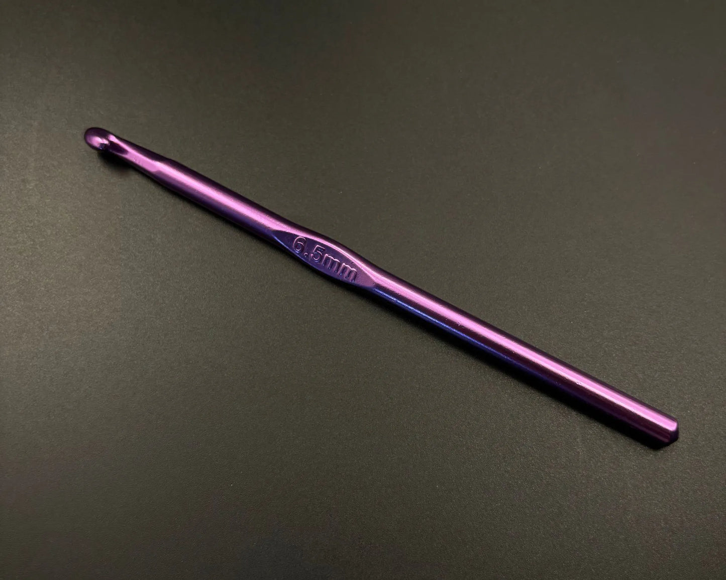 Single 6.5mm purple hook from rainbow aluminum crochet hooks set on black background