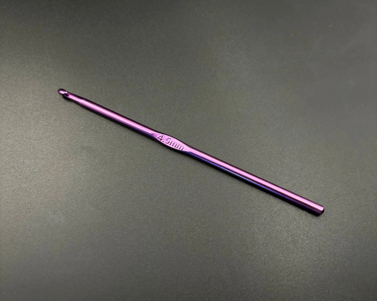 Single purple crochet hook from the rainbow aluminum crochet hooks set on a dark background
