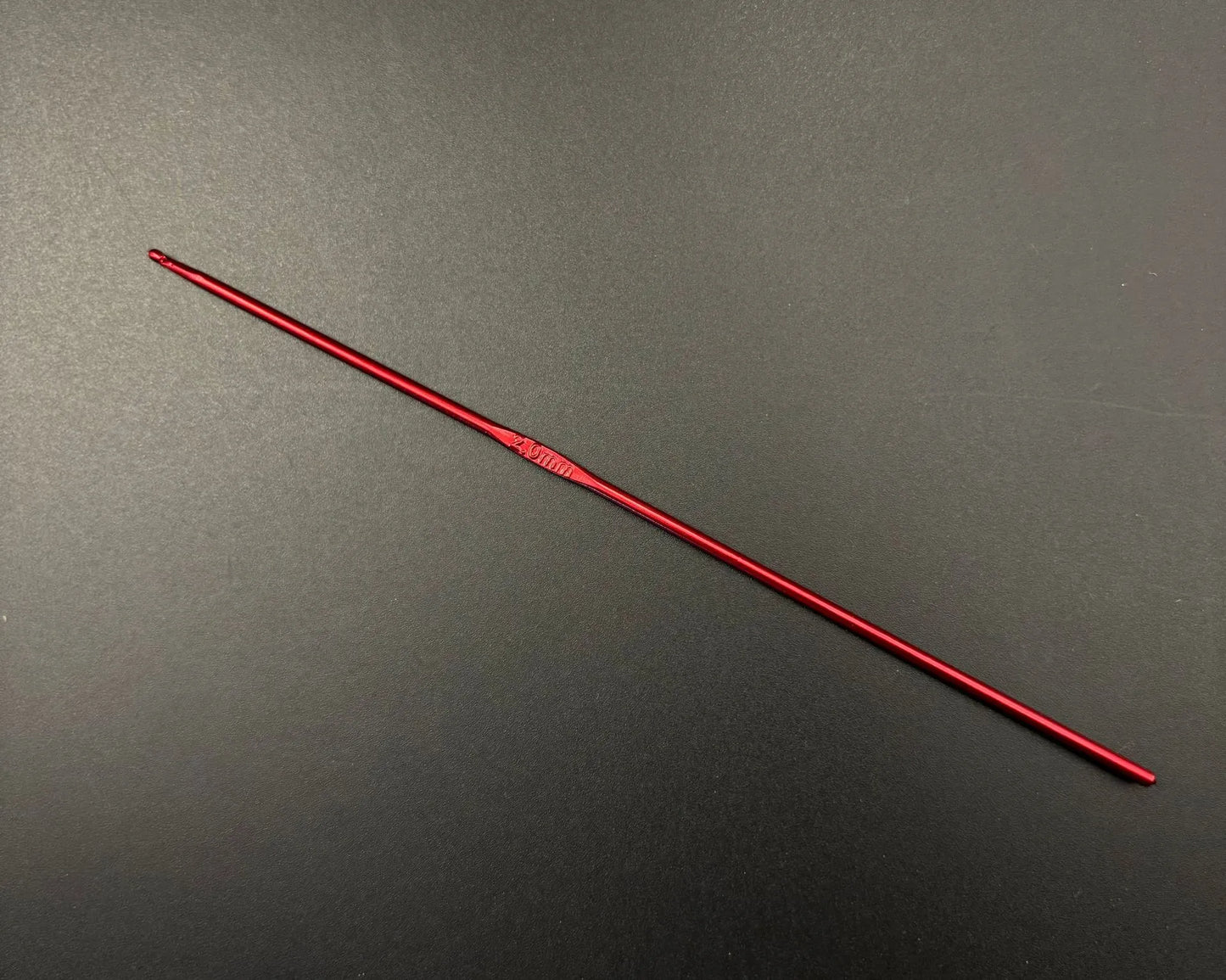 Single red crochet hook from rainbow aluminum crochet hooks set on black background
