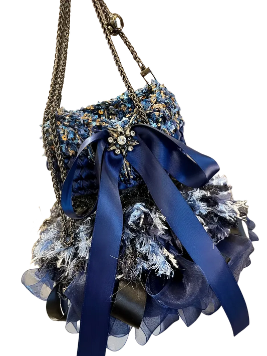 Detailed blue crochet handbag pattern featuring textured yarn and decorative blue ribbon with chain handles