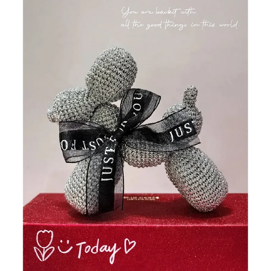 Crochet balloon dog pattern in gray yarn with black ribbon tied around the neck displayed on red surface