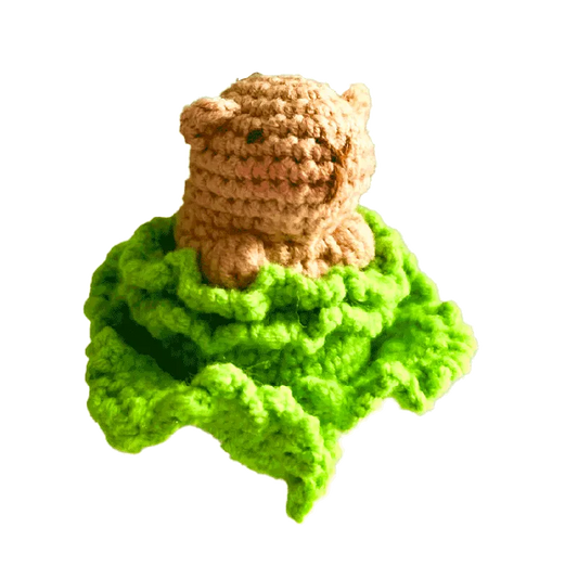 Small brown crocheted capybara sitting on bright green crochet leaves using crochet capybara pattern