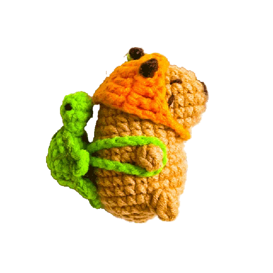 Handcrafted crochet mini capybara pattern with orange hat and green turtle backpack on black background