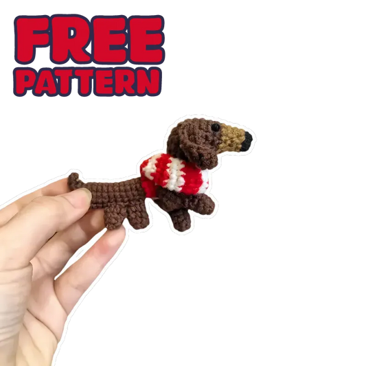 Hand holding a crochet DIY dachshund amigurumi with a red and white striped sweater on black background