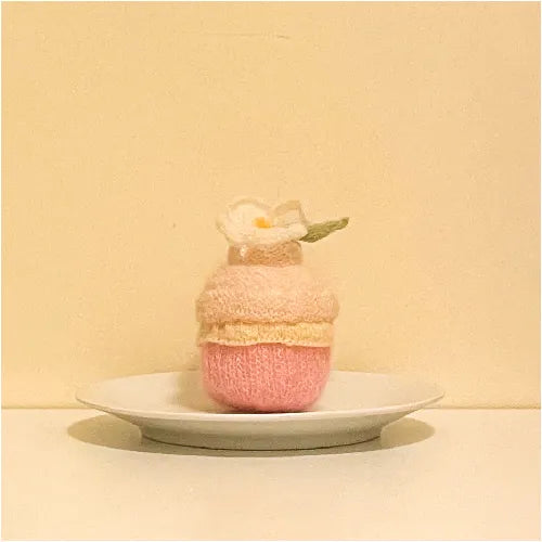 Handcrafted knitted cupcake pattern in pastel pink and cream colors displayed on a white plate