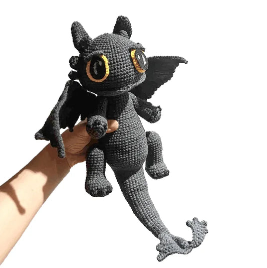 Hand holding a handmade Toothless crochet gift featuring black dragon with big yellow eyes and wings