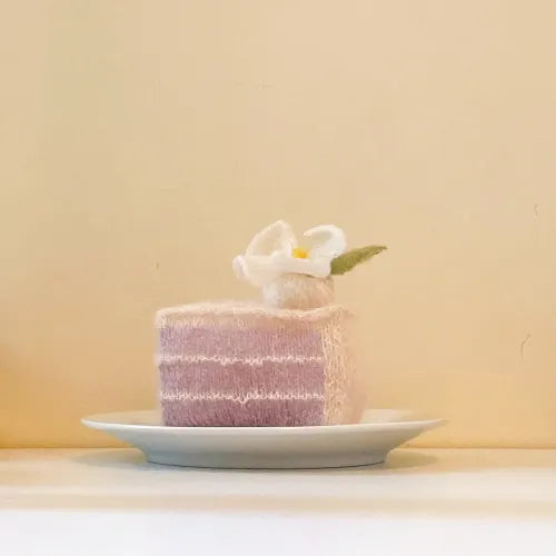 Soft pink knitted dessert pattern cake slice with white flower decoration on a white plate