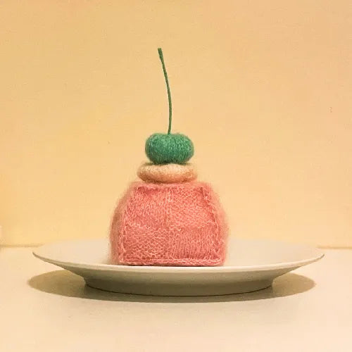 Knitted petit cake pattern soft pink square cake with green cherry on white plate