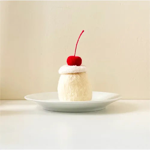Handmade knitted pudding pattern with a red cherry on top displayed on a white plate