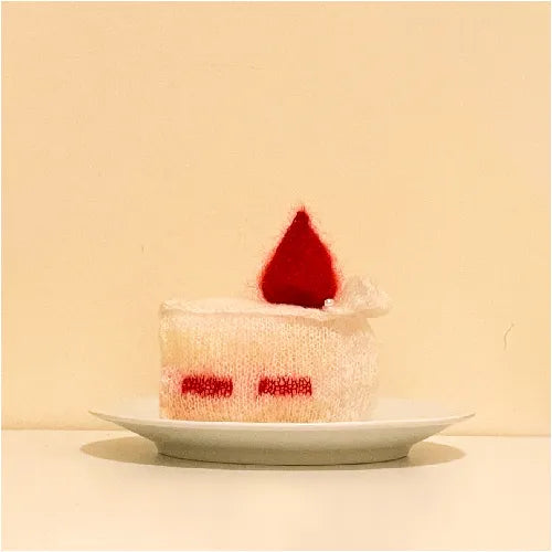 Cream-colored knitted strawberry cake pattern with red strawberry on top displayed on white plate