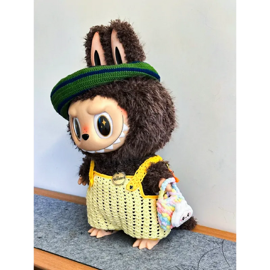 Cute toy figure wearing green headband and yellow Zimomo crochet outfit pattern overalls with plush brown fur